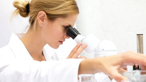 Junge Frau in weißem Kittel schaut in Mikroskop