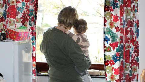 Wir sehen den Rücken einer der inhaftierten Frauen mit ihrem Kleinkind auf dem Arm. Beide gucken aus dem Fenster.  