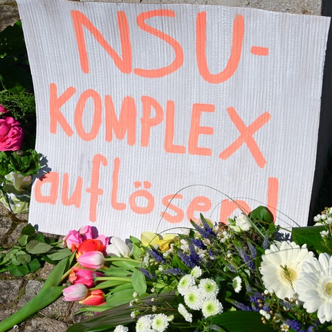 "NSU-Komplex auflösen" steht auch einem Karton, der inmitten das Blumenmeer an einem Gewdenkort gestellt wurde.