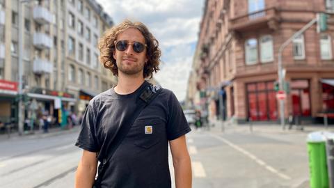 Streetworker Kevin arbeitet seit zwei Wochen bei WESER5. Mann mit Sonnenbrille und längeren lockigen Haaren steht im Frankfurter Bahnhofsviertel.