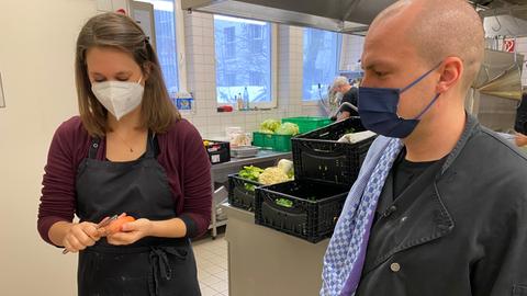 Reporterin Selina Rust und Helfer Jan Hoffmann schälen Karotten in einer Obdachlosenküche in Frankfurt