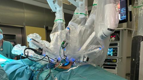 Operations-Roboter "DaVinci" hängt mit 4 in steriler Folie verpackten Armen über dem Bauch der Patientin im OP-Saal. 
