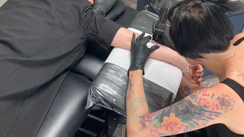 Eine Tätowiererin mt bunten Tattoos auf den Armen bei der Arbeit