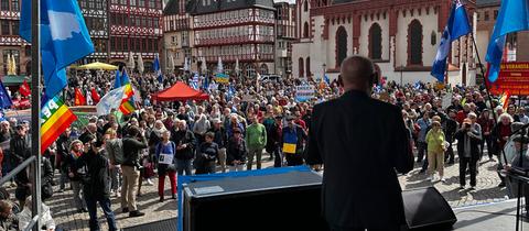 Vor dem Frankfurter Rathaus stehen hunderte Menschen mit bunten Fahnen bei einer Kundgebung.