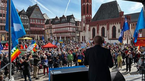 Vor dem Frankfurter Rathaus stehen hunderte Menschen mit bunten Fahnen bei einer Kundgebung.