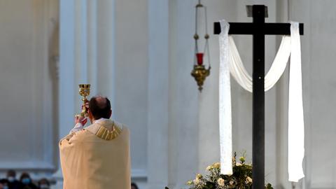 Ein katholischer Geistlicher steht am Altar neben einem Kreuz mit weißem Tuch.