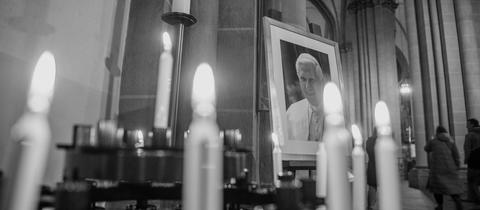 Portraitbild von Papst Benedikt XVI. steht zwischen Kerzen in einer Kirche.