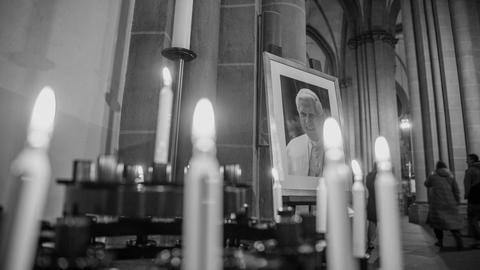 Portraitbild von Papst Benedikt XVI. steht zwischen Kerzen in einer Kirche.