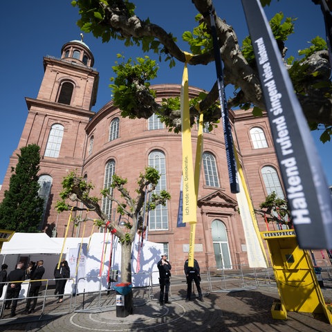 Vor der Paulskirche in Frankfurt sind Bäume mit bunten Bändern geschmückt.