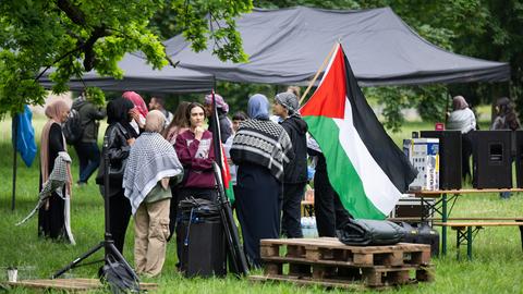 Teilnehmer an einem Pro-Palästina-Protestcamp auf dem Uni-Campus in Frankfurt, Menschen mit Palästina-Flagge und Palästinenser-Tüchern stehen vor einem Zelt