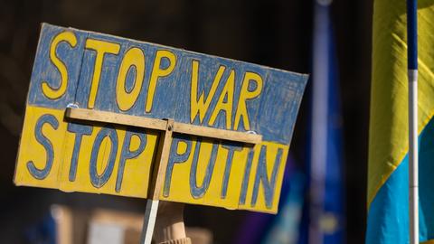"Stop War - Stop Putin" steht auf einem gelb-blauen Schild bei einer Demonstration. Daneben eine ukrainische Flagge.