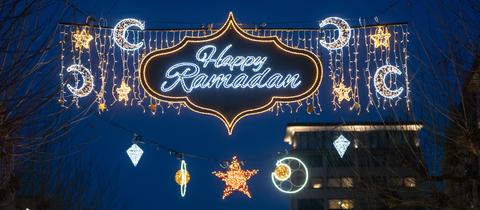 Sterne, Monde und der Schriftzug "Happy Ramadan" leuchten bei Einbruch der Dunkelheit über der Frankfurter "Fressgass'". 