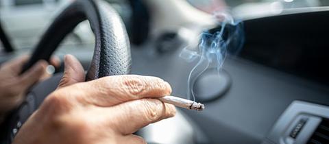 Ein Autofahrer mit qualmender Zigarette zwischen den Fingern
