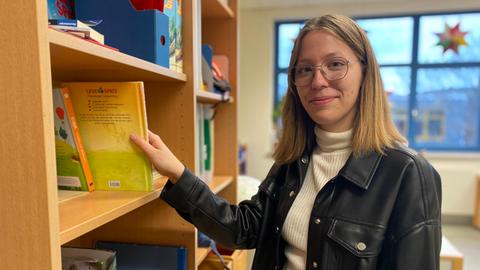 Rebecca Staier - sie macht gerade ein Freiwilliges Soziales Jahr. Frau mit halblangen blonden Haaren und Brille steht neben einem Bücherregal und nimmt ein Buch heraus.