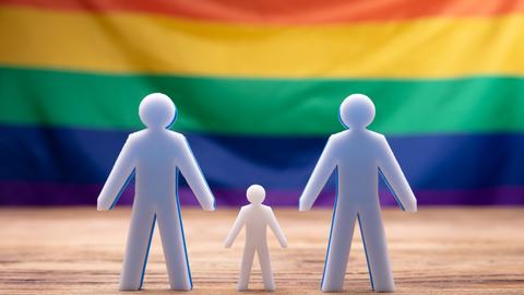 Figuren von zwei Männern und Kind vor Regenbogenfahne