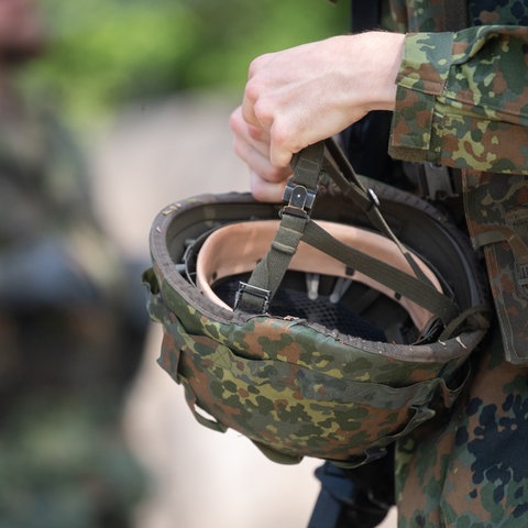 Ein Soldat präsentiert einen Helm im Tarnfleckmuster. 
