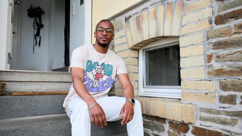 Ein schwarzer Mann Anfang 20, stitzt vor einem Haus auf einer Treppe
