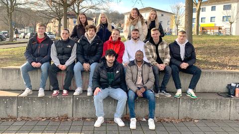Eine Schar junger Menschen sitzen unter Bäumen auf Stufen und posieren für das Foto.