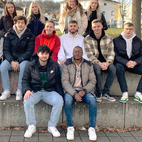 Eine Schar junger Menschen sitzen unter Bäumen auf Stufen und posieren für das Foto.
