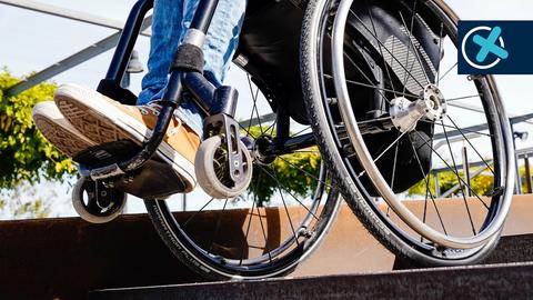 Rollstuhl mit Person in Nahaufnahme an einem Treppenabsatz - von unten fotografiert.