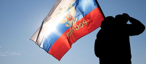 Ein Mann hält eine russische Fahne während einer Kundgebung zur Unterstützung Russlands. 