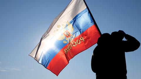 Ein Mann hält eine russische Fahne während einer Kundgebung zur Unterstützung Russlands. 
