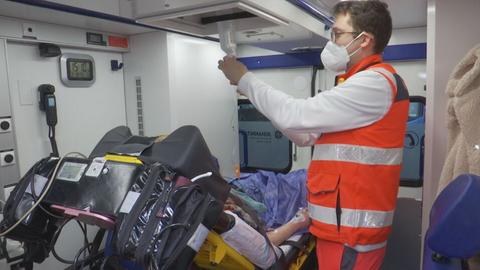 Ein Notfallsanitäter steht im Krankenwagen neben einer Patientin auf der Liege.