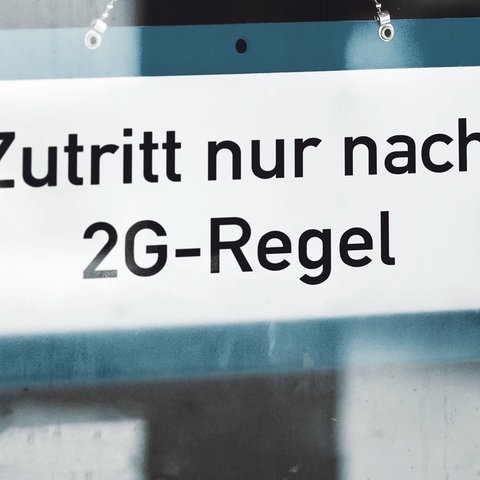 Schild mit der Aufschrift "Zutritt nur nach 2G-Regel", das an einer Glastür hängt.