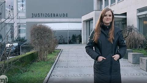 Eine junge Frau steht vor einem Gerichtsgebäude und lächelt