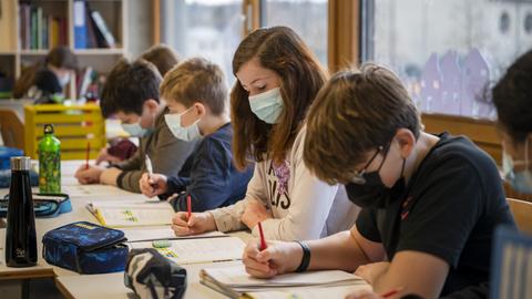 Schülerinnen und Schüler sitzen am Schreibtisch im Klassenzimmer und targen Masken.