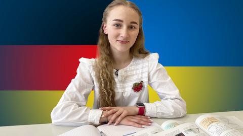 Im Bildvordergrund sitzt eine junge Frau an einem Tisch hinter Schulbüchern. Im Bildhintergrund auf der einen Seite die deutsche Flagge, auf der anderen Seite die ukrainische Flagge.