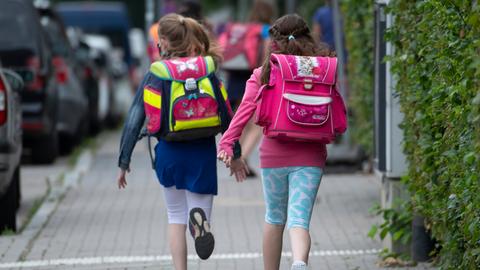 Zwei Schülerinnen einer Grundschule rennen mit einem Schulranzen auf dem Rücken die letzten Meter bis zum Schulhof. 
