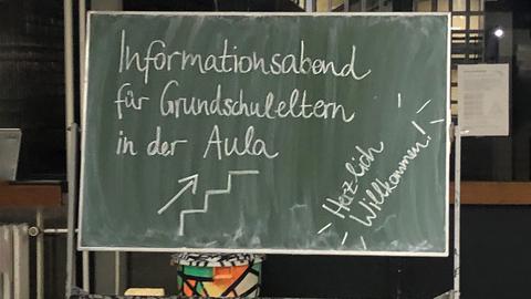 Kreidetafel mit Schrift: "Informationsabend für Grundschuleltern in der Aula. Herzlich Willkommen!"