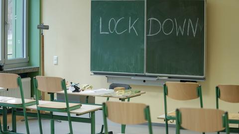 Die Stühle im Klassenraum sind hochgestellt, auf der Tafel steht mit Kreide das Wort "Lockdown".