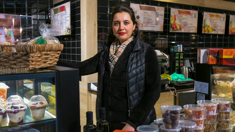 Geschäftsfrau Serpil Aydin steht hinter dem Tresen ihres "Saftladens". In der Auslage sind Salate und belegte Brötchen zu sehen.