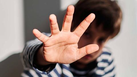 Eine abwehrende Hand eines Jungen vor seinem Gesicht, das unscharf im Bildhintergrund zu sehen ist.