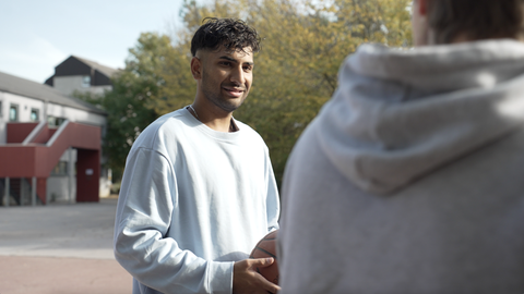 Ali Mahmood, lächelnder junger Mann mit weißem Sweatshirt und lockiger Kurzhaarfrisur
