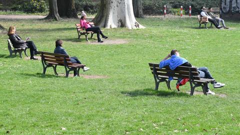 In einem Park sitzen Menschen vereinzelt auf fünf Bänken.
