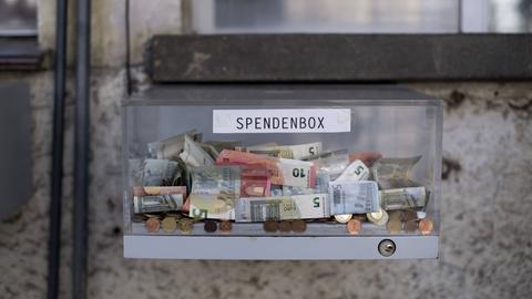 Transparente Box mit Geldmünzen und Geldscheinen - mit der Aufschrift "Spendenbox"