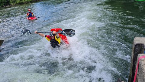 Ein Kanufahrer in einem roten Wildwasserkajak macht gerade einen Salto im Wasser