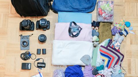 Teile einer Kameraausrüstung, Decken, Baby-Kleidung und Unterlagen liegen auf einem Boden.