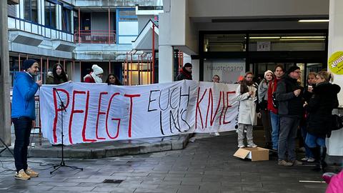 Streikende am UKGM in Marburg halten ein Banner mit der Aufschrift "Pflegt euch ins Knie".