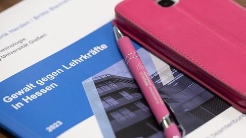Ein Stift und ein Smartphone in der Farbe Rosa liegen währen einer Vorstellung der Studie "Gewalt gegen Lehrer" des Deutschen Beamtenbundes (dbb) Hessen auf einer Zusammenfassung der Studie.