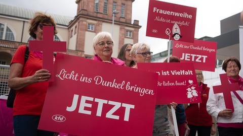 Mehrere Frauen halten rosafarbene Plakate und Kreuze hoch, auf denen unter anderem die Aufschrift "Licht ins Dunkel bringen" steht.