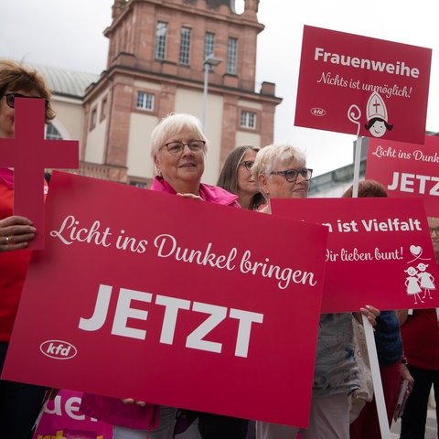 Mehrere Frauen halten rosafarbene Plakate und Kreuze hoch, auf denen unter anderem die Aufschrift "Licht ins Dunkel bringen" steht.