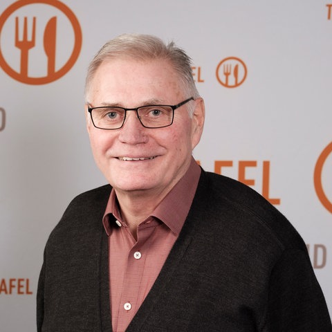 Willi Schmid schaut in die Kamera, hinter ihm eine Wand mit dem Schriftzug "Tafel Hessen"