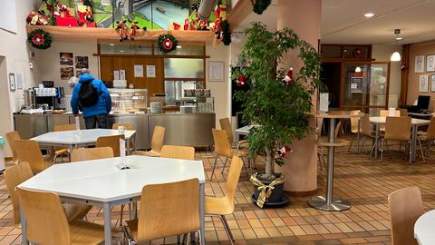 Der Innenraum der Tagesaufenthaltsstätte Panama in Kassel mit Holzstühlen und Tischen, im Hintergrund die Essensausgabe, an der ein Mann ansteht.