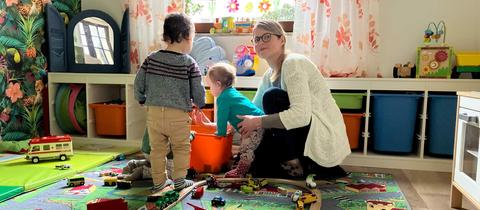 Foto einer Frau, die mit zwei Kindern auf dem Boden sitzt und spielt.