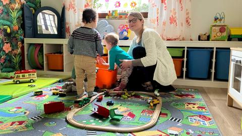 Foto einer Frau, die mit zwei Kindern auf dem Boden sitzt und spielt.