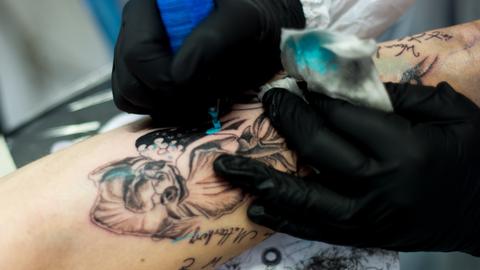 Tätowiererin fertigt an einem Unterarm ein Tattoo